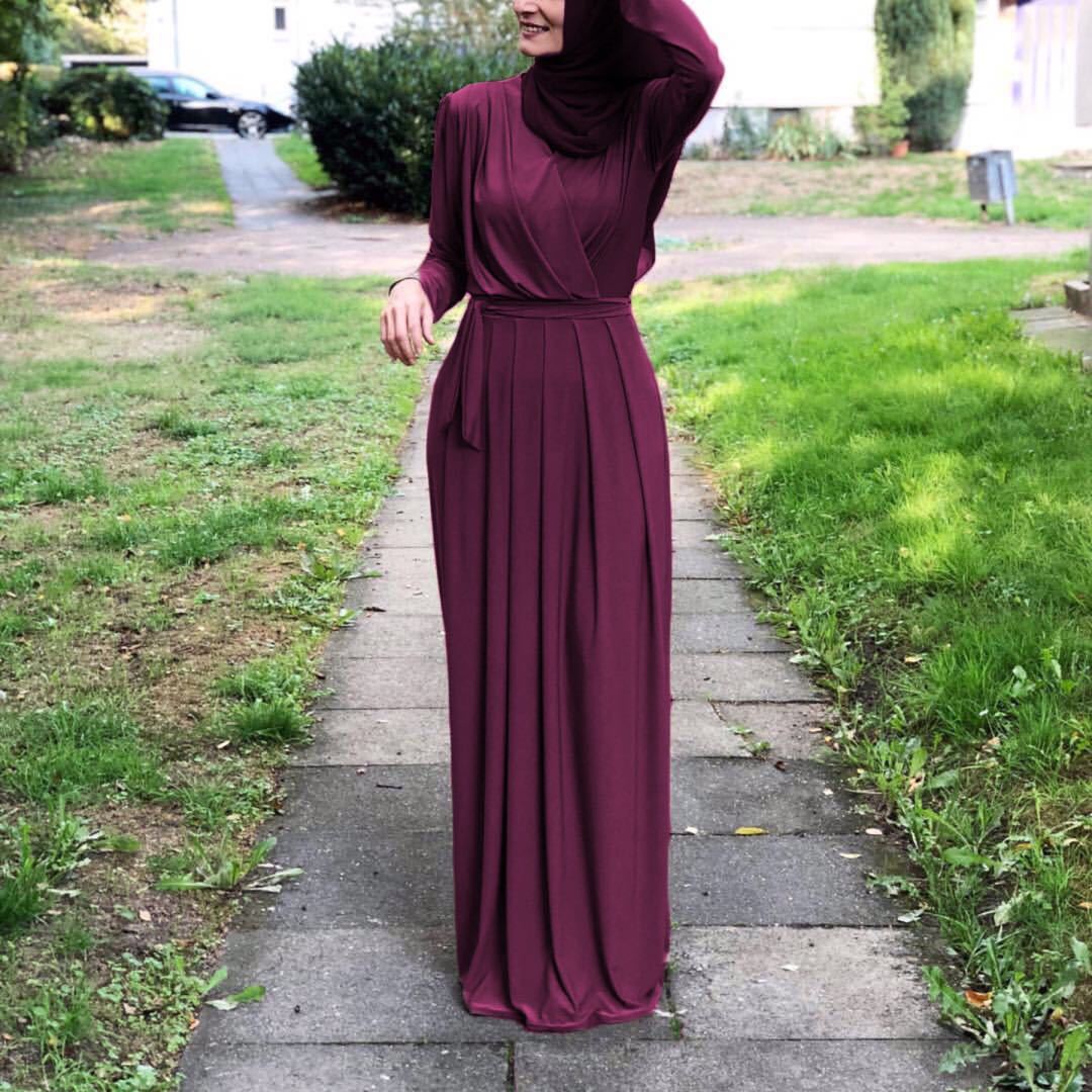 Flowy milk silk abaya dress in burgundy worn by a woman in a garden setting, highlighting elegance and modesty.