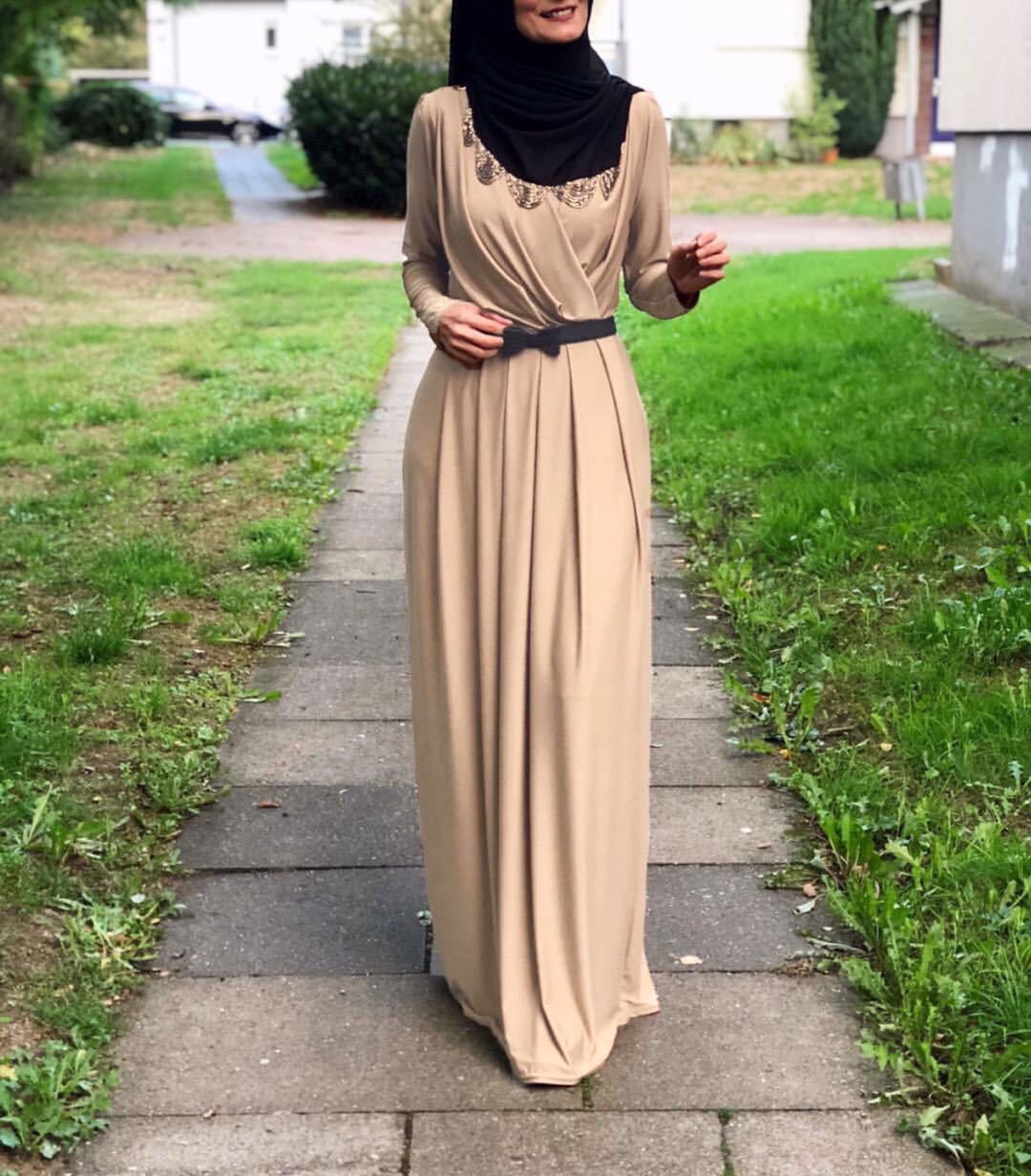 Woman in beige flowy milk silk abaya dress with black belt, showcasing elegant modest fashion on a path.